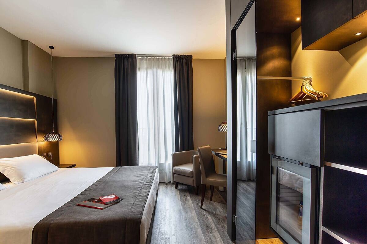 A modern hotel room with a large bed, a desk, and a minibar.