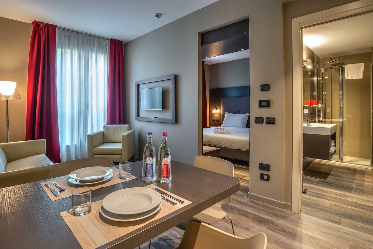 A hotel room with a dining area, a bed, a bathroom, and a TV.