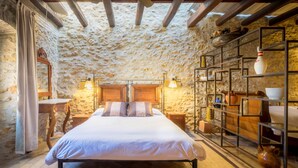 A rustic bedroom with a stone wall, wooden bed, and shelves with pottery. - CAN FELIP Apartment with Fantastic Views (Palafrugell)