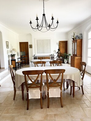 A dining area with a chandelier, wooden chairs, a round table, and a cabinet with decorative items.