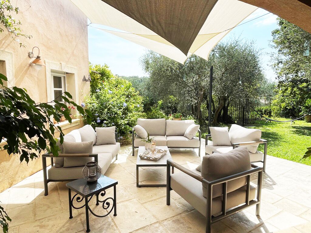 Une terrasse extérieure avec un ensemble de meubles de jardin de couleur beige, une table basse et un vase décoratif.