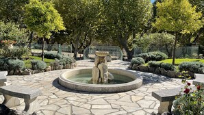 A stone fountain with a statue in the center, surrounded by a stone-tiled patio and various shrubs and trees. - Large air-conditioned family villa with private pool in Provence, French Riviera (Le Rouret)
