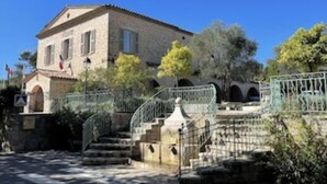 A stone building with a tiled roof, a staircase leading to an entrance, and a metal gate. - Large air-conditioned family villa with private pool in Provence, French Riviera (Le Rouret)