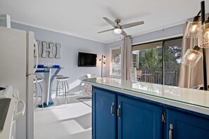 A modern kitchen with a blue cabinet, a glass-top island, and a ceiling fan. - Just Beachy, Ocean View, steps to the beach, and Walking to Shopping and Dining🏖️ (Hilton Head Island)