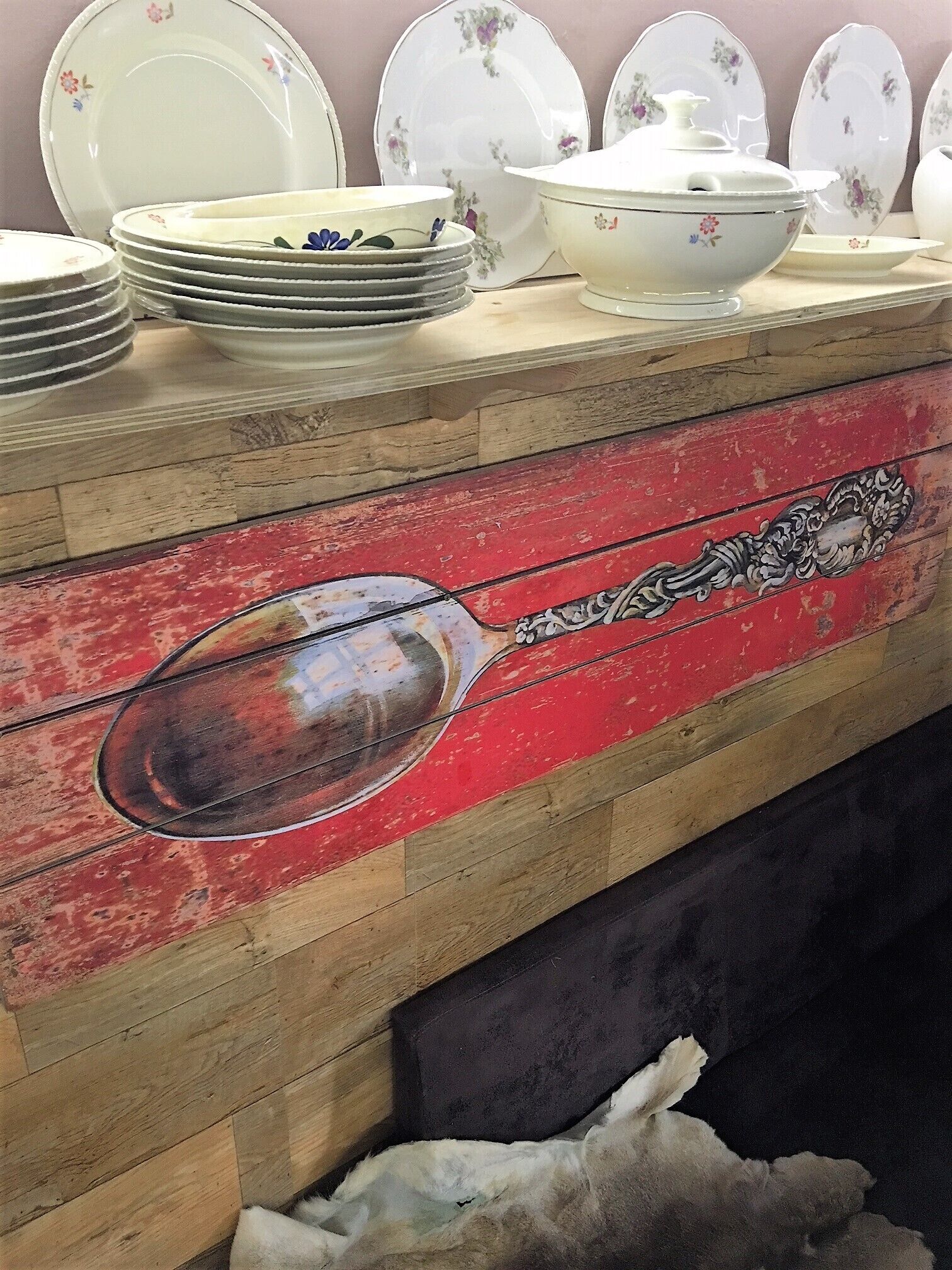 Un meuble en bois orné d’un motif décoratif en forme de cuillère, avec des assiettes empilées et un bol blanc à motifs floraux.