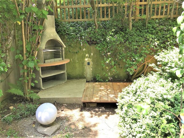 A garden with a stone barbecue area, a wooden deck, and a spherical sculpture.