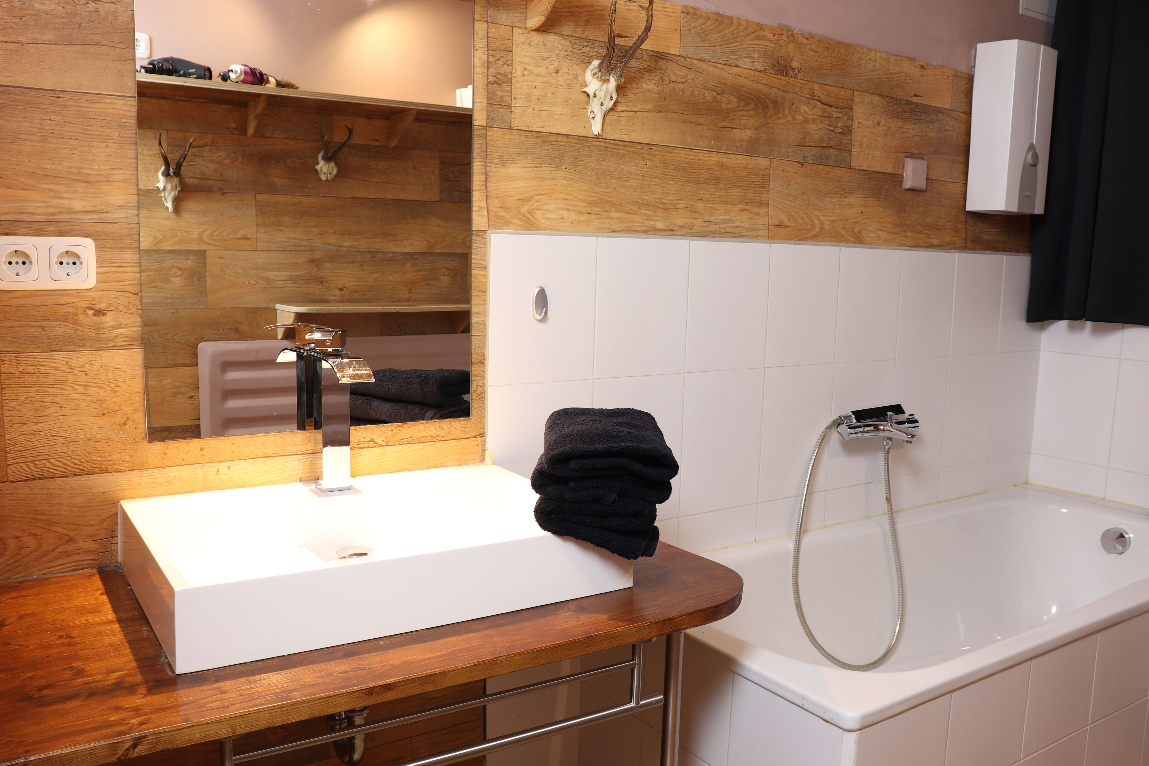 A bathroom with a wooden vanity, a sink, a mirror, a towel, and a bathtub with a showerhead.