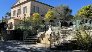 A stone building with a tiled roof, a staircase leading to an upper level, and a flag on the building. - Flat duplex in Villa  4/6 pers. Near Grasse, Swimming pool, Garden (Le Rouret)