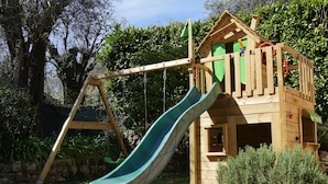A wooden playhouse with a slide and a swing set in a garden. - Flat duplex in Villa  4/6 pers. Near Grasse, Swimming pool, Garden (Le Rouret)