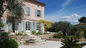 A two-story house with a stone staircase leading to the entrance, surrounded by lush greenery and a well-maintained garden. - Flat duplex in Villa  4/6 pers. Near Grasse, Swimming pool, Garden (Le Rouret)