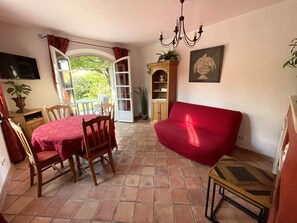 A dining area with a table and chairs, a red sofa, a wooden cabinet, and a potted plant.