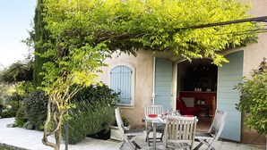 A patio with a table and chairs, a hanging vine, and a building entrance. - Flat duplex in Villa  4/6 pers. Near Grasse, Swimming pool, Garden (Le Rouret)