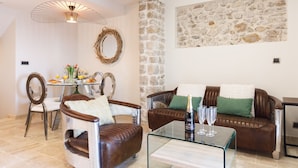 A cozy living room with a stone wall, a dining area with a table and chairs, and a leather sofa with cushions. - First-Row Sea View Retreat · Old Town Antibes · 2BR with Balcony (Antibes)