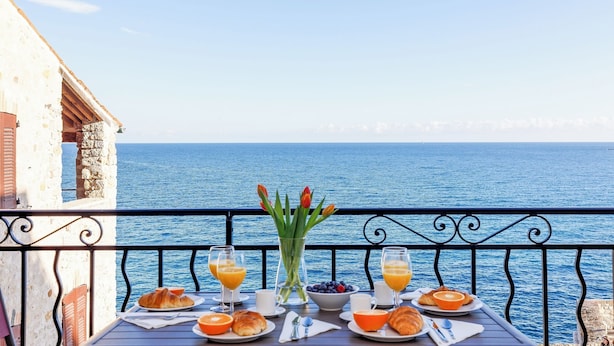 A balcony table with breakfast items, a vase of flowers, and a view of the sea. - First-Row Sea View Retreat · Old Town Antibes · 2BR with Balcony (Antibes)