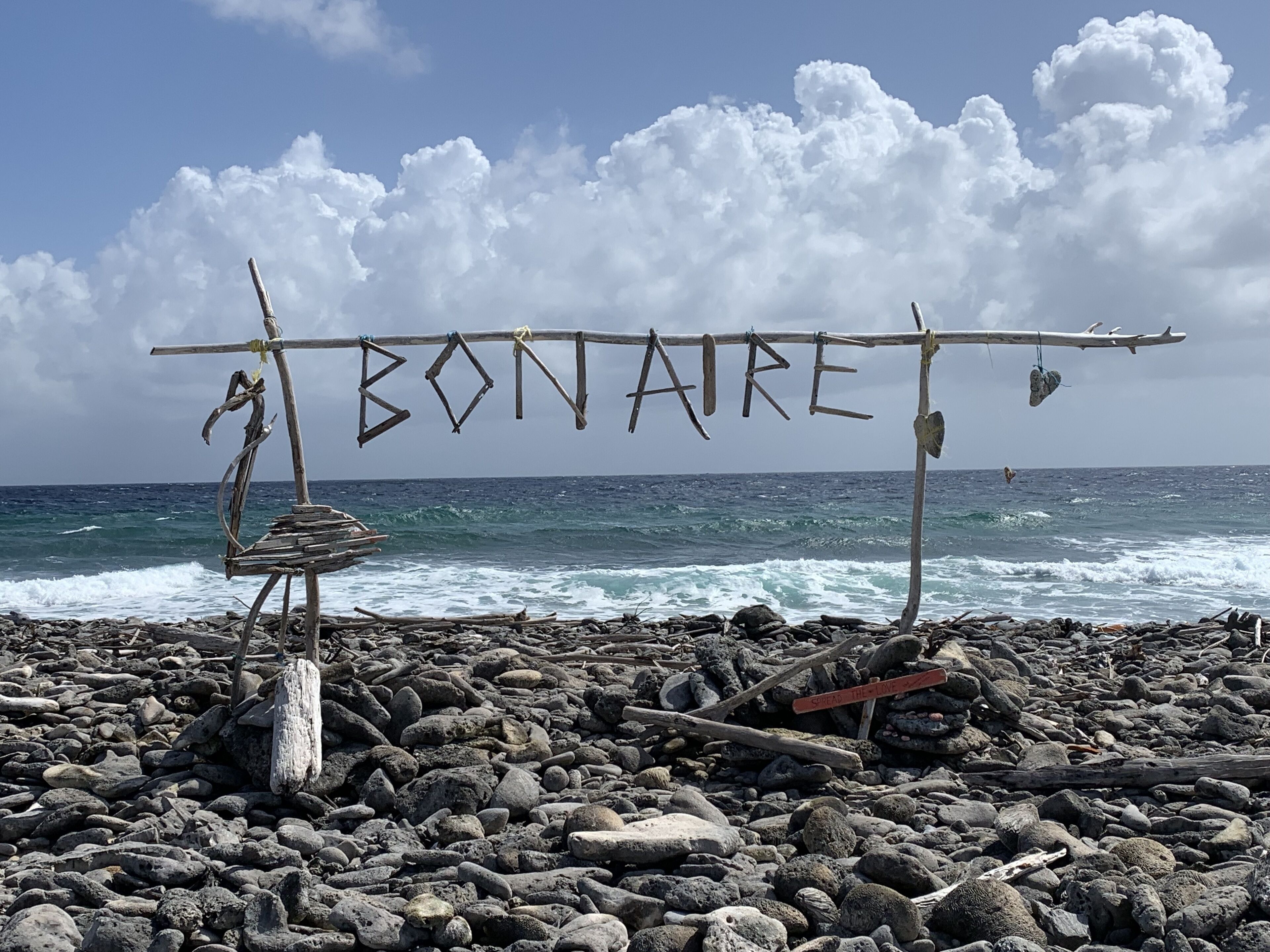 Une plage avec un panneau en bois sur lequel on peut lire « BONARE » et un autre panneau qui indique « ACCÉLÉREZ L’AMOUR ».