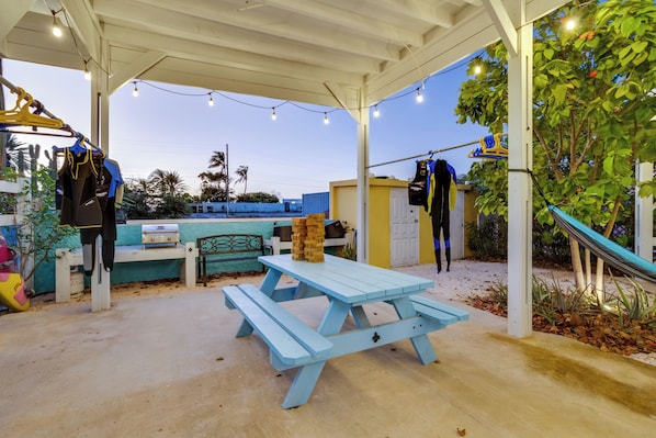 A covered outdoor area with a picnic table, hanging clothes, and a slide.