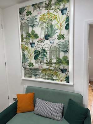 A room with a green sofa, a patterned wall, and a window with a view.