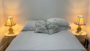 A neatly made bed with two pillows, two bedside lamps, and a small table with a cup. - A Newly Refurbished Apartment in Notting Hill, London (London)