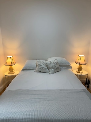 A neatly made bed with two pillows, two bedside lamps, and a small table with a cup.
