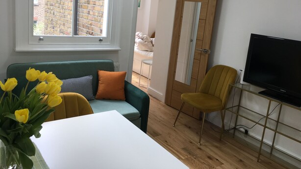 A living room with a green sofa, a yellow chair, a white table, and a TV on a stand. - A Newly Refurbished Apartment in Notting Hill, London (London)