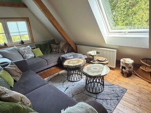 A cozy loft bedroom with a sloped ceiling, a gray sofa, a wooden floor, and a large window overlooking greenery. - Eulennest Apartment in an idyllic, detached, and modern forest cottage (Forbach)