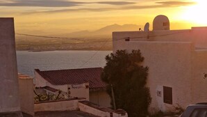 Un edificio costiero con tetto in tegole rosse, un'antenna parabolica e vista sul mare e sulle montagne sullo sfondo.
