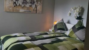 Una camera da letto con un letto, una ventola a soffitto, un quadro appeso al muro e un vaso con fiori.