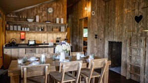 Un interior rústico de madera con una mesa de comedor para cuatro, una zona de cocina con armarios de madera y una chimenea con un recorte en forma de corazón.