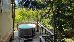 Un jacuzzi en una terraza de madera con barandilla, rodeado de abundante follaje.