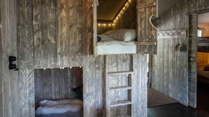 Una habitación rústica con cama en entrepiso, escalera y un pequeño rincón para dormir.