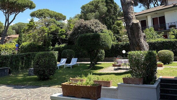 A well-maintained garden with various trees and shrubs, outdoor seating, and a paved pathway. - RED 1 Apartment (Portiglioni)