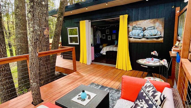 A cozy outdoor seating area with a wooden deck, a sofa with patterned cushions, and a table with a decorative item. - 3 River Cabins - Private Group Retreat - Downtown Sparta! (North)