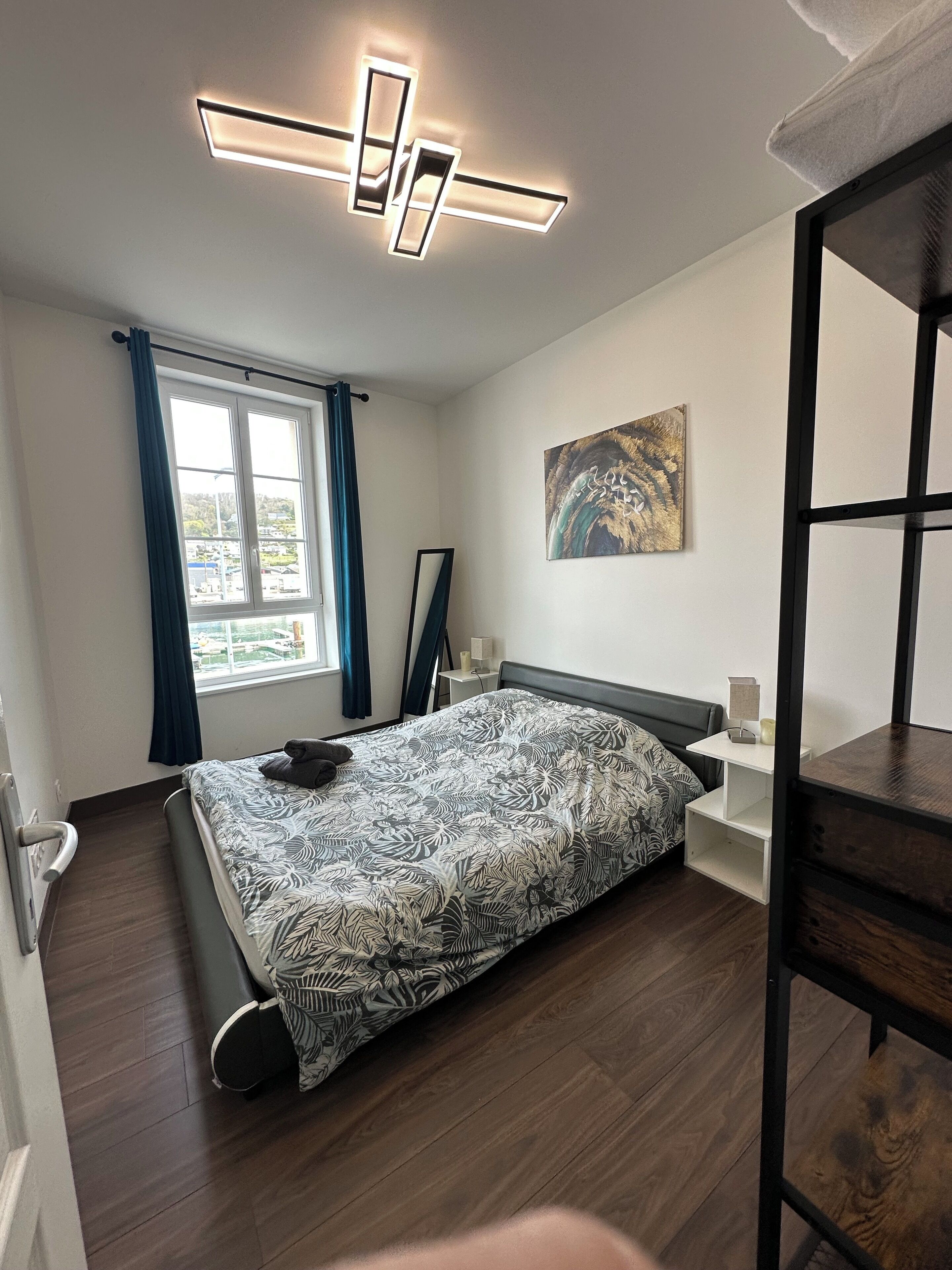 Ein modernes Schlafzimmer mit Bett, einem Fenster mit Vorhängen, einem Bild an der Wand und Holzboden.