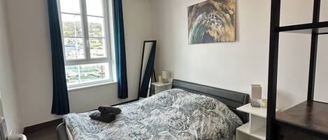 Ein modernes Schlafzimmer mit Bett, einem Fenster mit Vorhängen, einem Bild an der Wand und Holzboden.