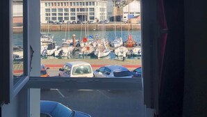 A view through a window of a marina with boats, a building with a sign, and a car in the foreground. - Captain YOO - Bénéc - App Industriel sur le Port (Fécamp)