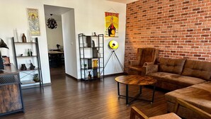 A living room with a brick wall, a sofa, a coffee table, and a bookshelf. - Captain YOO - Bénéc - App Industriel sur le Port (Fécamp)