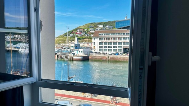 A room with a large window overlooking a marina, a dock, and a building with a white facade.