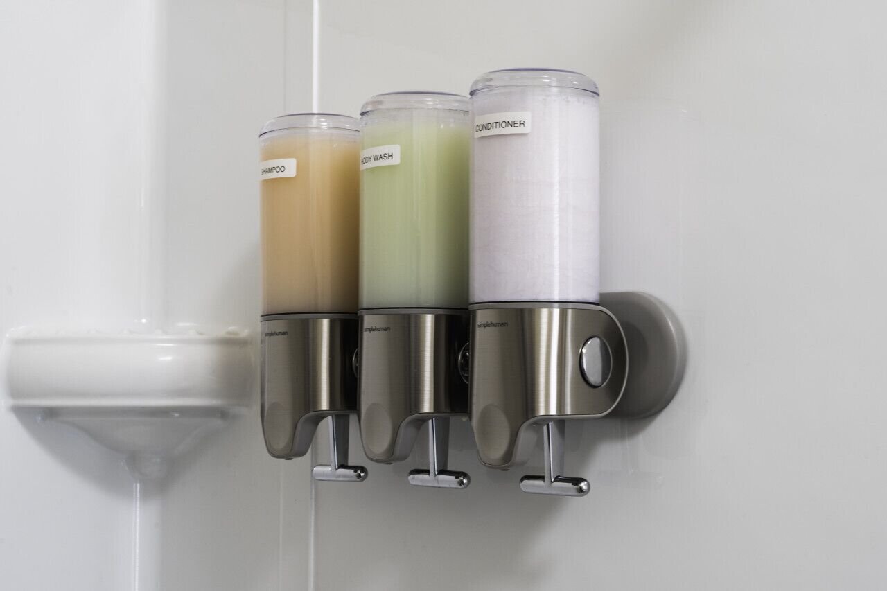 A wall-mounted dispenser with three compartments labeled shampoo, body wash, and conditioner.