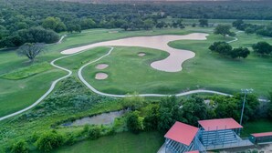 An aerial view of a golf course with sand bunkers, a pond, and a building with a red roof. - 4 Queen Beds | High Speed Wifi (Fort Worth)