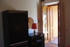 Ein Zimmer mit einem großen, dunkelbraunen Schrank, einem kleinen Tisch mit roter Lampe und einer Tür zu einem Außenbereich mit Holzläden.