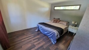 A bedroom with a bed, a nightstand, a window, and a wooden floor. - La Tribu, House with pool and whirlpool, ideal for families (Sierra de los Padres)