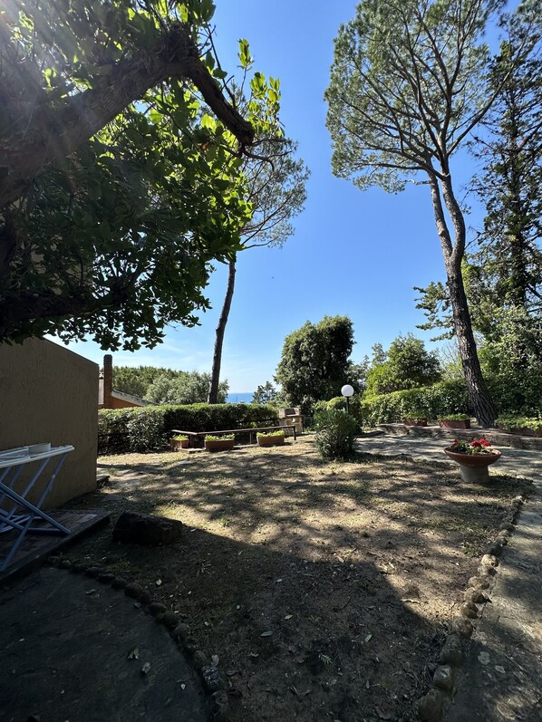 A garden with a variety of trees and potted plants, a small table, and a bench. - AZURE 2 Apartment (Portiglioni)