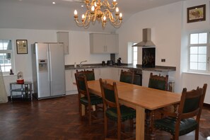 A modern kitchen with a dining area, featuring a chandelier, wooden dining table, and green upholstered chairs. - Indoor heated pool, games room and tennis court all private. (Caergwrle, North Wales)