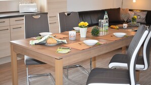 A modern dining area with a wooden table, black and white chairs, and a kitchen in the background. - 5-star apartment, 60 sqm, 2nd floor, family-friendly, WiFi, playground in the garden  (Bad Brambach)