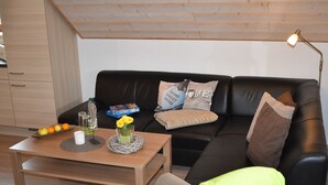 A modern living room with a wooden coffee table, a black leather sofa, and a small side table. - 5-star apartment, 60 sqm, 2nd floor, family-friendly, WiFi, playground in the garden  (Bad Brambach)