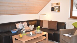 A cozy living room with a wooden ceiling, a black leather sofa, a wooden coffee table, and a green armchair. - 5-star apartment, 60 sqm, 2nd floor, family-friendly, WiFi, playground in the garden  (Bad Brambach)