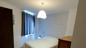 Una camera da letto con pavimento in legno, un letto con copriletto bianco, una lampada a sospensione e una finestra con tende.