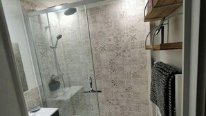 Una doccia a pavimento con piastrelle decorate, una porta in vetro e un lavandino bianco con un mobile scuro.
