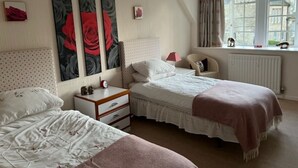 Een slaapkamer met twee bedden, een nachtkastje, een dressoir en een raam met gordijnen.