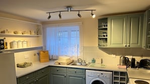 Een keuken met groene kastjes, een wasmachine, een fornuis en een raam met gordijnen.